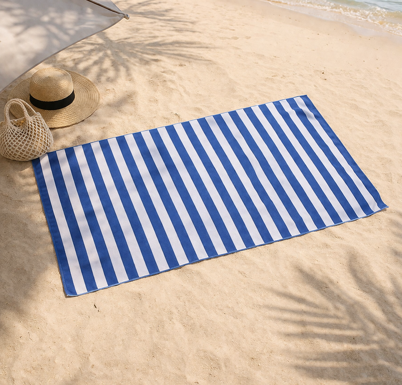 Blue and white striped towel on a sandy beach with a hat and bag nearby.