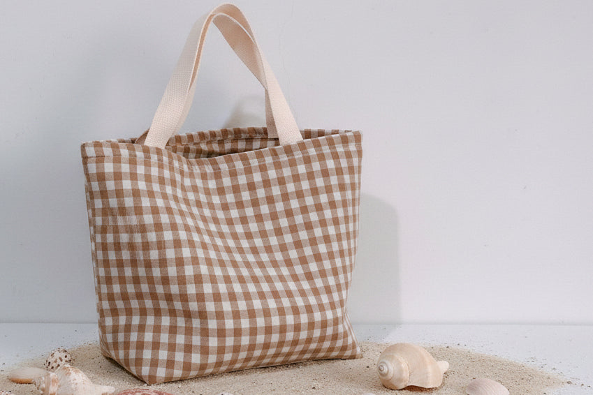 Brown and white checkered tote bag next to a book on a light gray surface with a light gray background