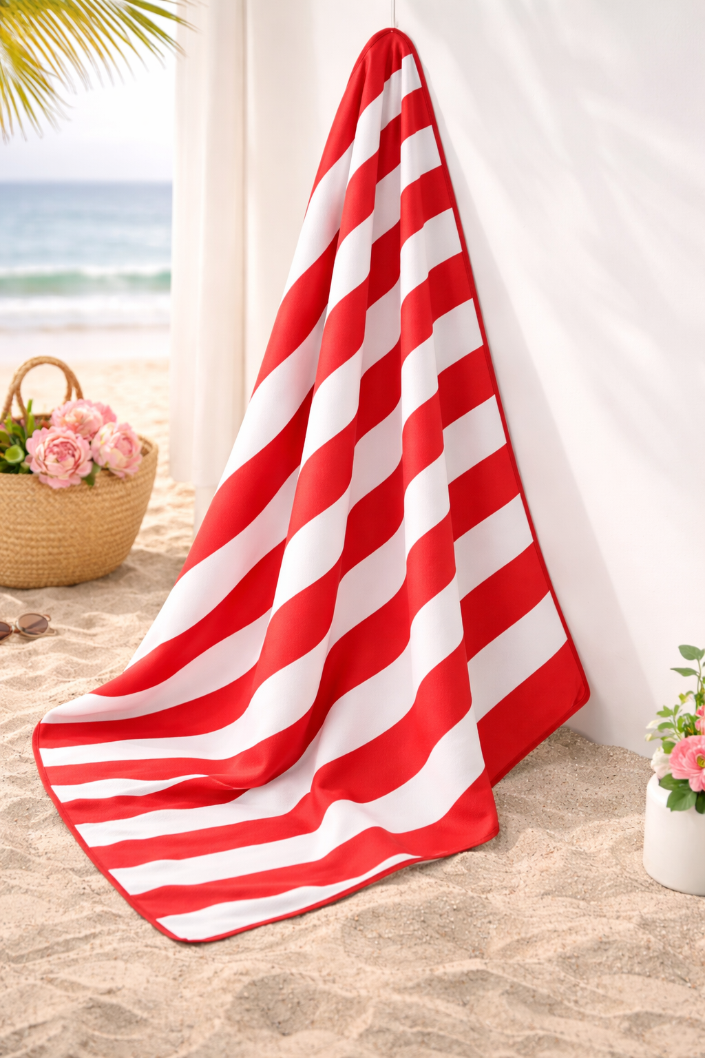 Red and white striped towel on a sandy surface with beach elements in the background