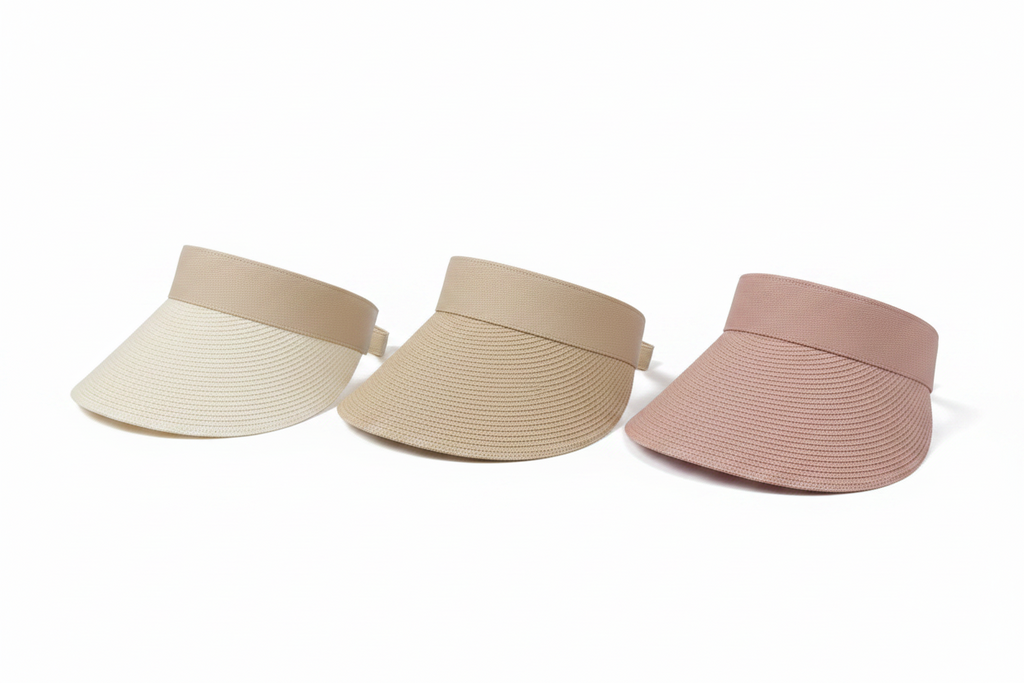 Two straw visors, one beige and one pink, on a white surface with a woven basket in the background.