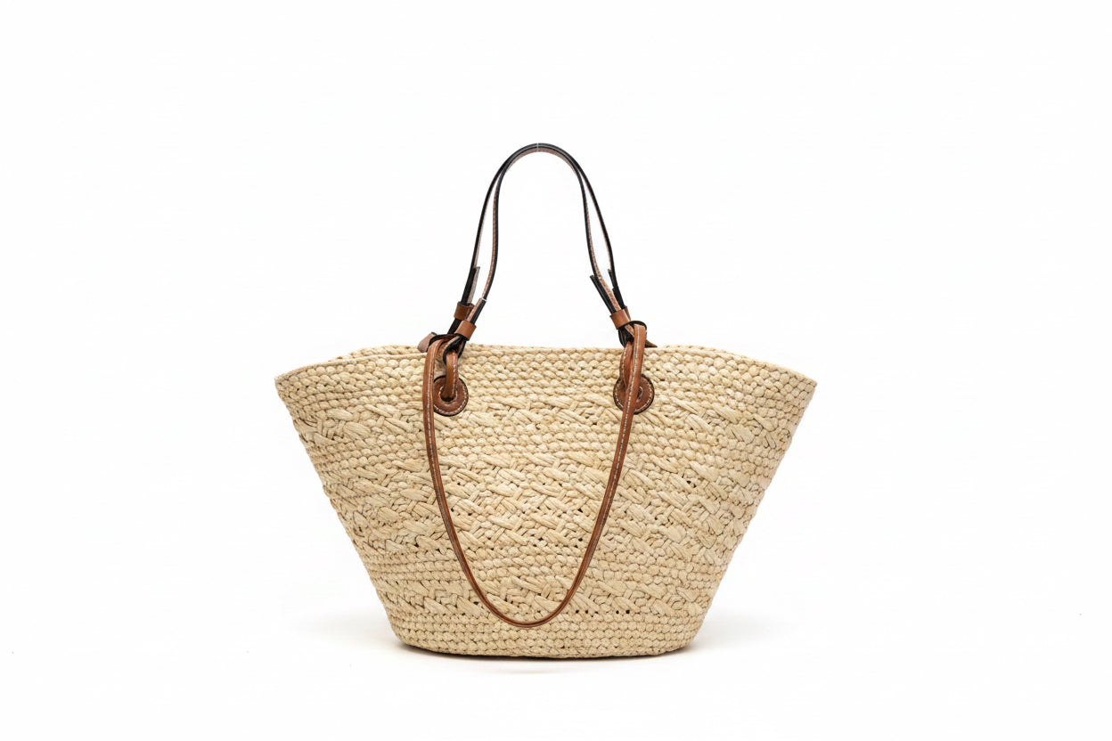 Woven handbag with brown handles on a black surface against a white wall.